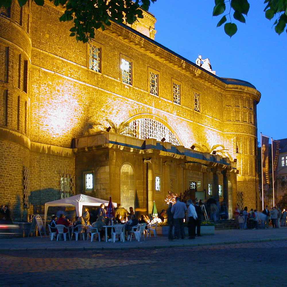 Außenansicht des Landesmuseums für Vorgeschichte Halle bei Nacht. Viele Menschen sitzen auf Stühlen vor dem Gebäude.
